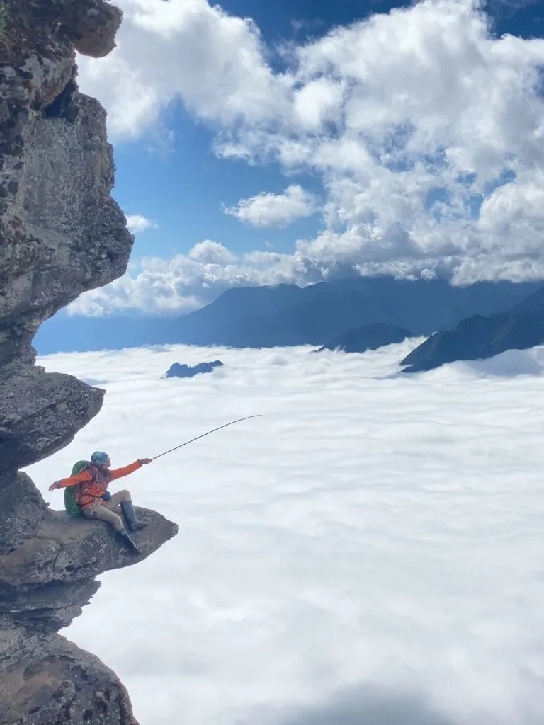 Person sitting on a rocky outcrop overlooking clouds