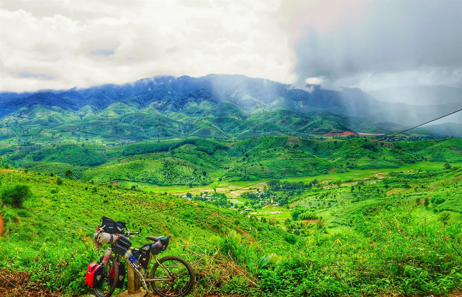 A group of motorbikes traveling on a red dirt road towards the base of Mount Ngoc Linh, Kon Tum