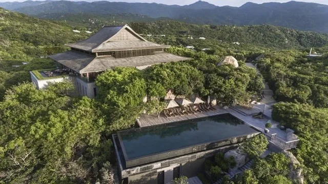 An aerial view of Amanoi Resort in Ninh Thuan, highlighting its luxurious pavilions and villas nestled within a lush landscape overlooking the bay, suggesting a heavenly retreat.