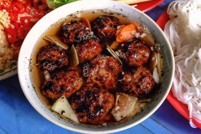 How to eat Hanoi bun cha by dipping vermicelli into a bowl of dipping sauce with grilled pork