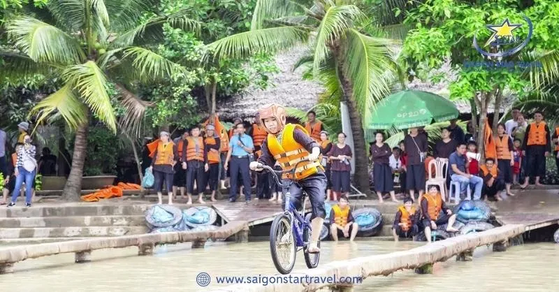 A person cycling on a narrow bamboo bridge over water, a folk game at Lan Vuong Ben Tre