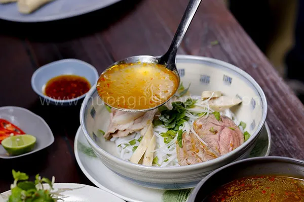 Adding ingredients to a bowl of Bun Bo Hue