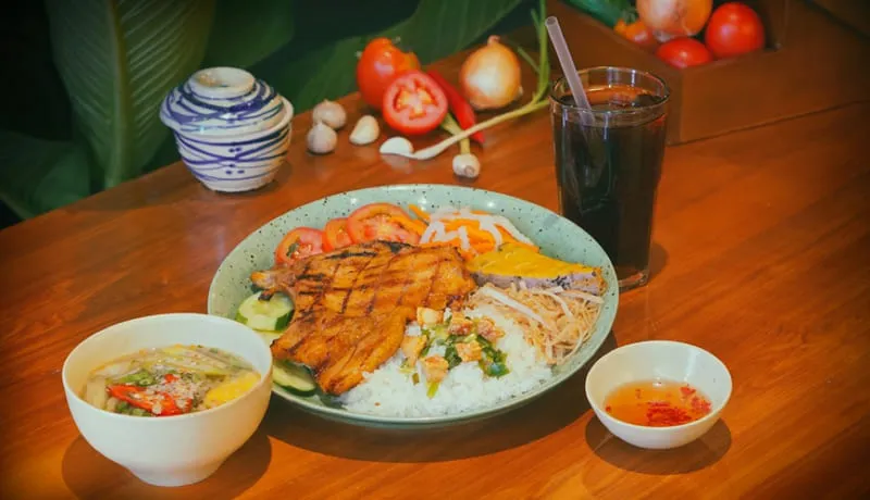A plate of Cơm Tấm Sà Bì Chưởng, a Saigon broken rice dish from a restaurant owned by famous streamers, featuring a variety of toppings.