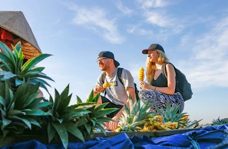 Foreign tourists experience eating pineapple on a boat at Can Tho floating market