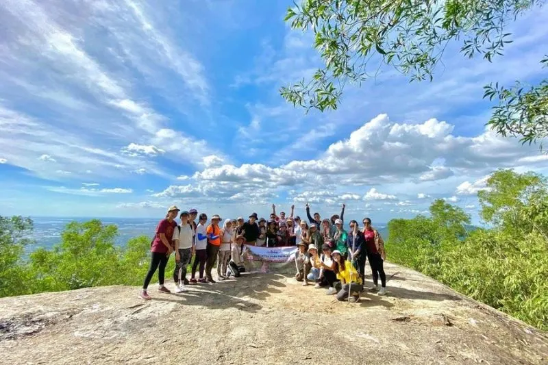 A group of hikers resting on large rocks at the summit of Nui Dinh overlooking the landscape