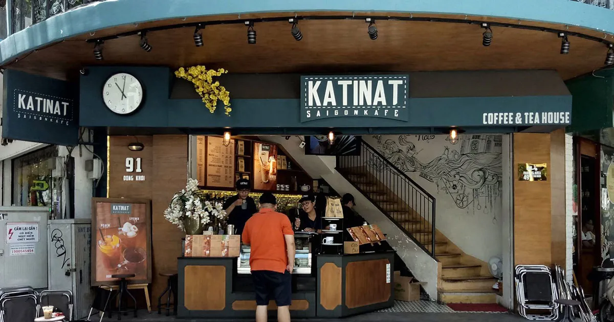Exterior view of Katinat Saigon Kafe at night, showing its modern design and outdoor seating area with city lights in the background.