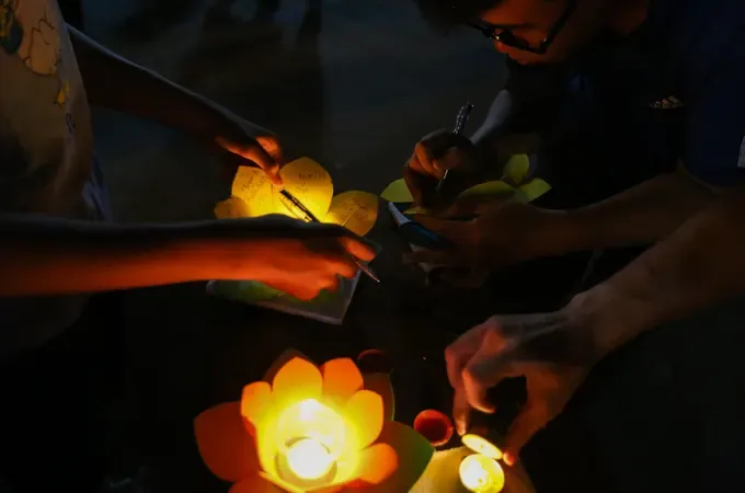 A hand releasing a flower lantern into the river, symbolizing sending wishes and prayers.