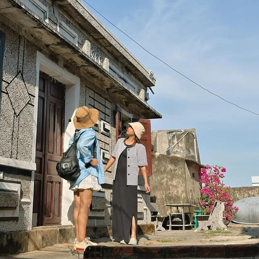 Young travelers taking photos in front of colorful old houses in Nhon Ly fishing village, Binh Dinh, Vietnam.