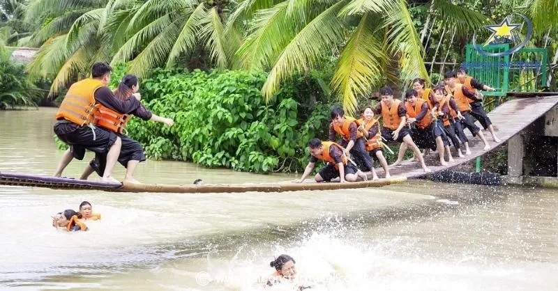 People playing on a wobbly wooden bridge over water, a balancing game in Ben Tre day tour